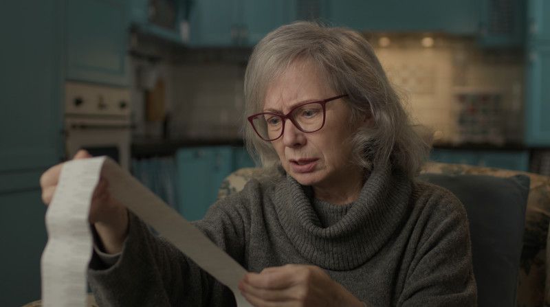 Elderly woman looks at a really long Farmers Market sales receipt.