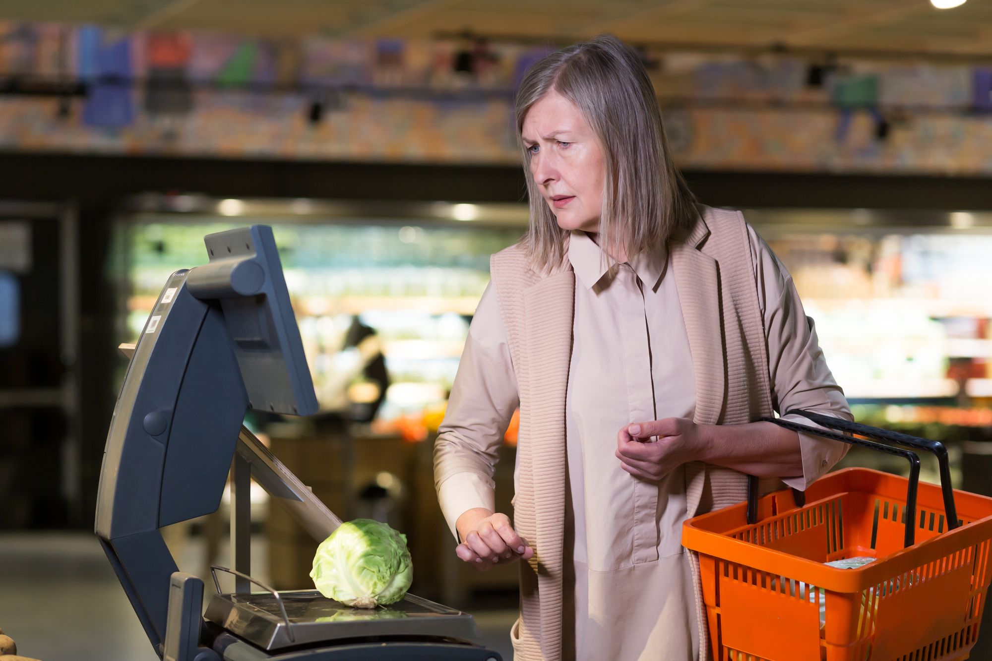 A woman carefully examining a cabbage in a grocery store, her expression showing concern about its quality and price.