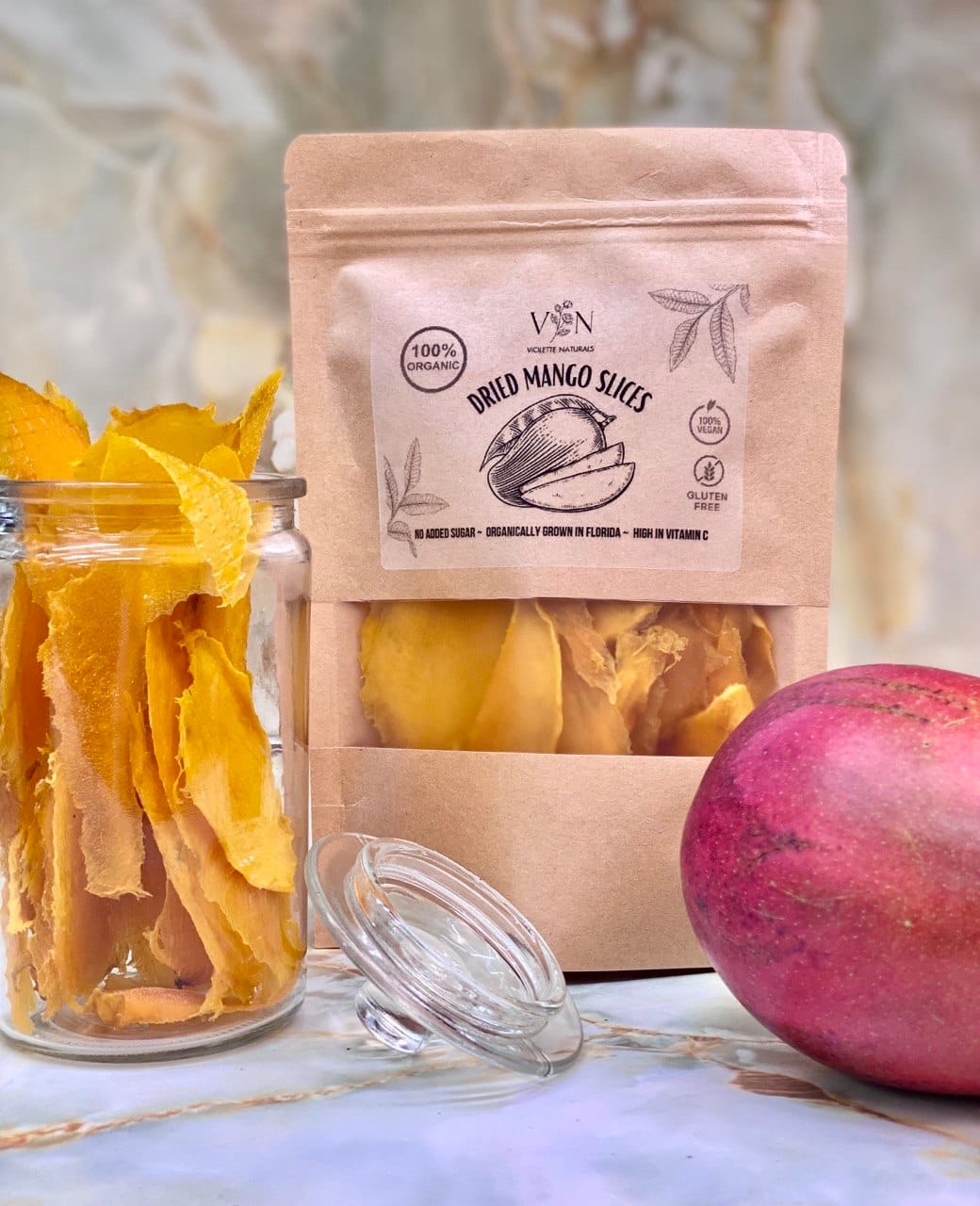 Bag of  dried mango slices next to a glass jar of dried mango and a fresh Florida mango